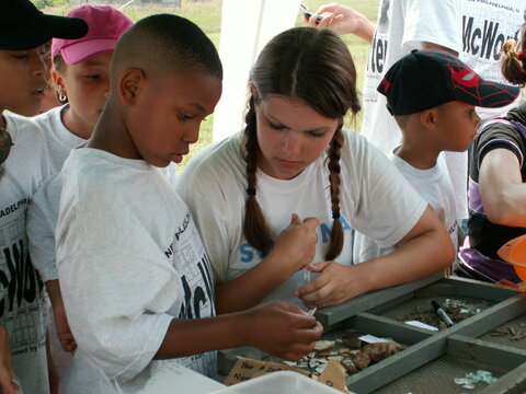 Children gather around looking at a table of material artifacts.