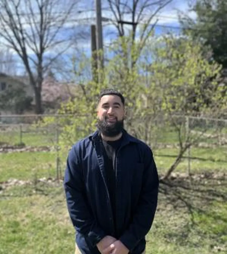 Omar Agustin Hernandez, Anthropology Graduate Student. A man stands, hands clasped, outside in a nature space.